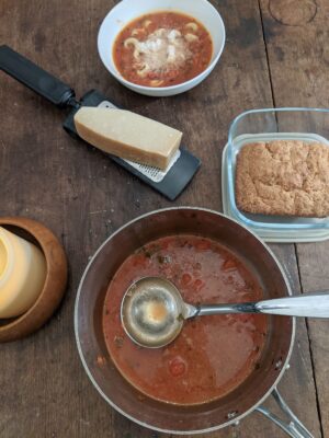 Rustic kitchen table with pot of Lasagna Soup, a block of parmesan cheese on a grater, some fresh bread