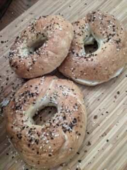 Three freshly baked homemade bagels on a wooden cutting board.